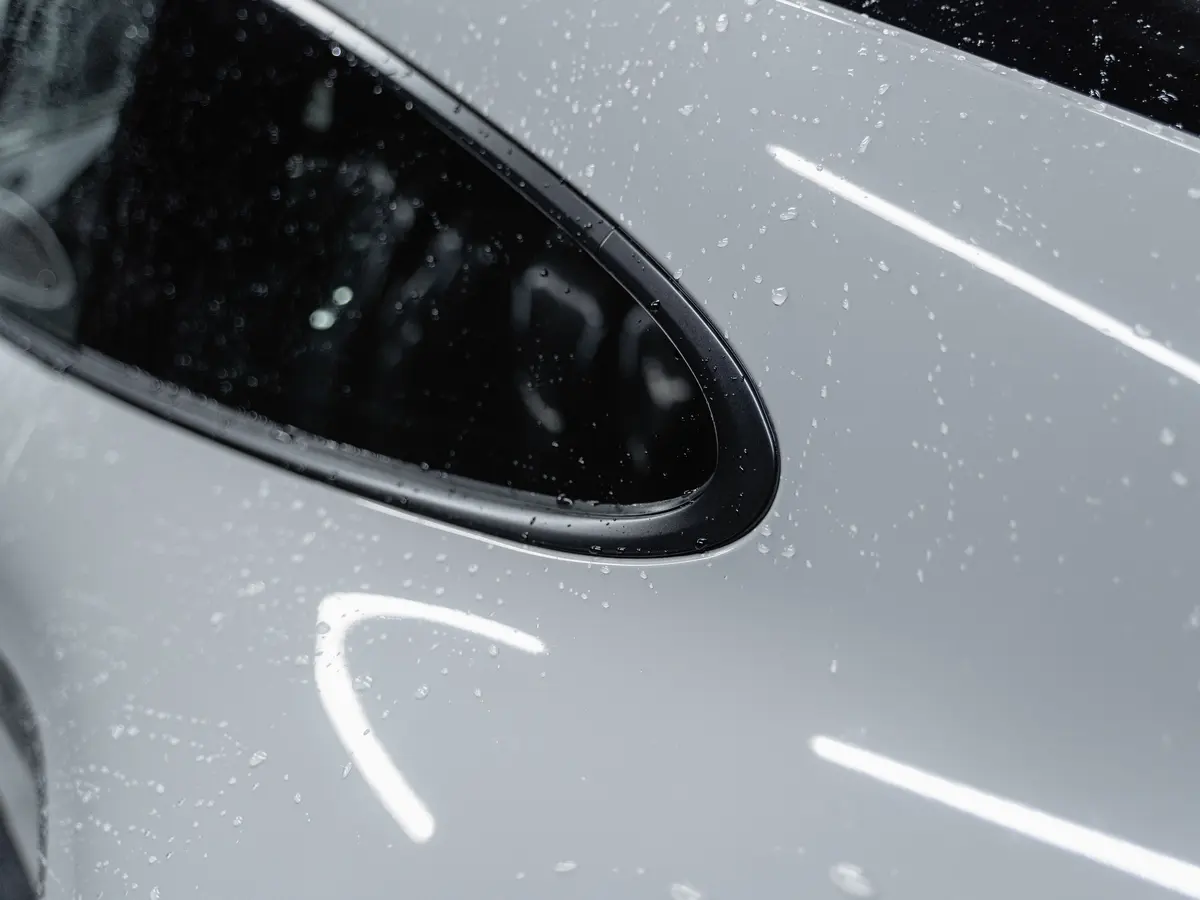 Water beading on silver car paint, with strip lights reflected in the panel